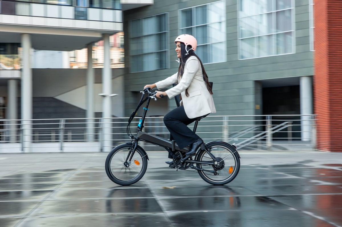 Businesswoman riding an electric folding bike on a city street — safe urban commuting